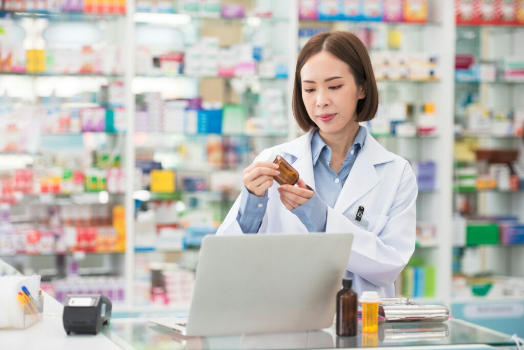 pharmacist asian woman smiling at counter using laptop computer for check medicine inventory